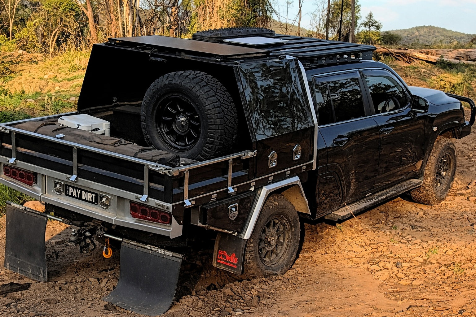 Black 300 series Landcruiser off-road vehicle with a roof rack and additional equipment on a dirt road.